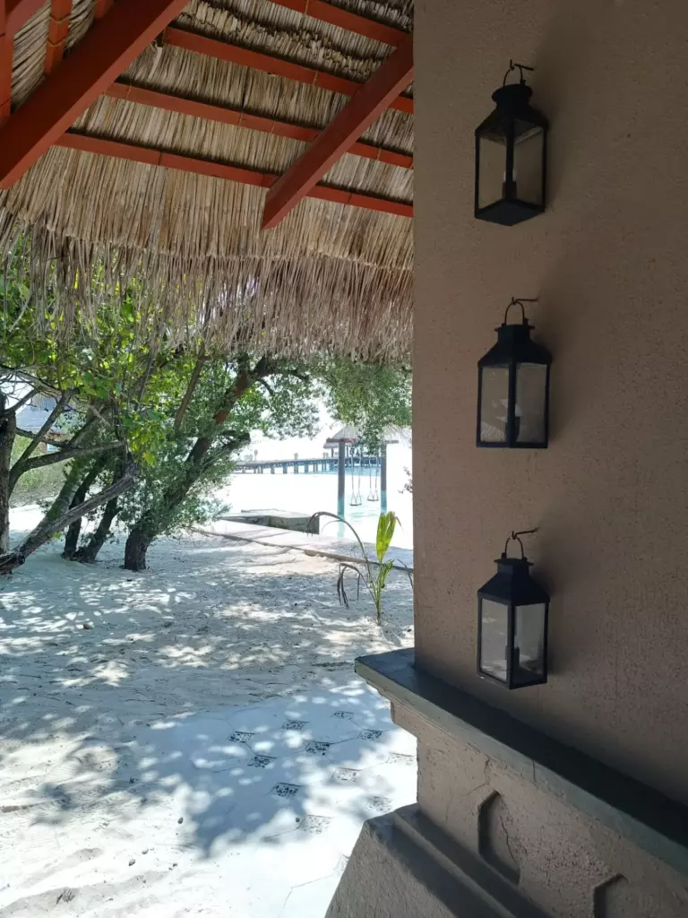 Lanterns on a wall under a thatched roof beside a beach in the Maldives