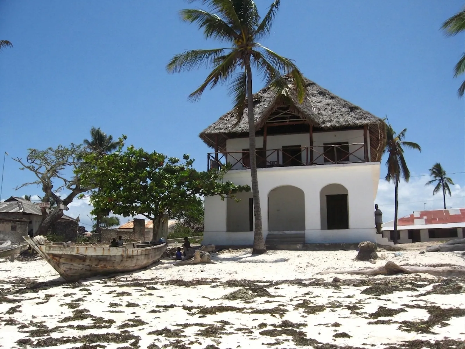 Swahili coastal house with thatched roof beside a wooden dhow on the sand